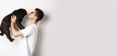 Yakışıklı bir gencin küçük şirin köpek suratını öptüğünün profili. Hippi adam köpeğini seviyor, beyaz arka planda duruyor..