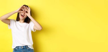 El dürbününden bakıp gülümseyen, sarı arka planda gezinen komik Asyalı kız..