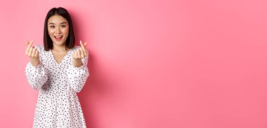 Koreli kalp işaretleri gösteren, gülümseyen, romantik pembe arka planda duran Asyalı güzel bir kadın..