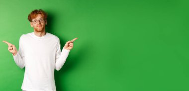 Kızıl saçlı kararsız komik adam kameraya şaşkın şaşkın bakıyor ve yeşil arka planda duran iki tanıtım teklifi sunuyor..