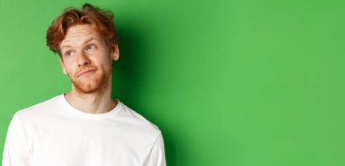 Saçları dağınık ve sakallı, gülümseyen kızıl saçlı adam, mutlu bir yüzle sola bakıyor, yeşil arka planda duruyor..