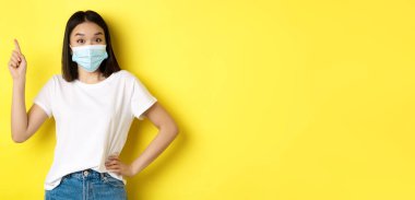 Covid, sağlık ve salgın hastalık konsepti. Tıbbi maskeli Asyalı kadın manken ve beyaz tişört sol üst köşedeki logoyu işaret ediyor..