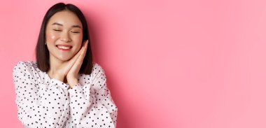 Güzellik ve yaşam tarzı konsepti. Güzel ve rüya gibi Asyalı bir kadının ellerinin üstünde uyuduğu, gözlerini kapadığı ve gülümsediği, pembe arka planda hayal kurduğu yakın plan..