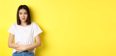 Asyalı bir kadının midesinde ağrı, karın ağrısı, acıdan çatık kaşlar, regl döneminde rahatsızlık, sarı arka planda durması..