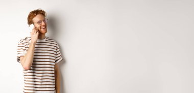 Cep telefonuyla konuşan, sola bakıp gülümseyen, beyaz arka planda duran mutlu genç adamın profili..