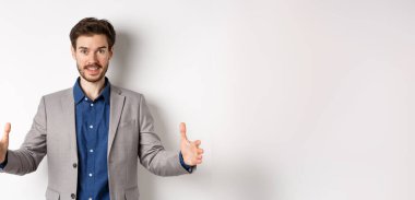 Heyecanlı yakışıklı iş adamı uzun boyda bir şey gösteriyor. Ellerini uzatıp beyaz arka planda duran büyük bir nesne..