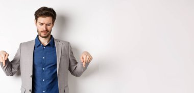 Etkilenmemiş genç işadamı hayal kırıklığına uğradı, kötü terfiyi işaret etti ve hor gördü, beyaz arka planda hoşnutsuzdu..