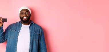 Alışveriş konsepti. Bereli memnun genç sakallı adam. Kredi kartı gösteriyor. Gülümsüyor..