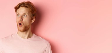 Şok olmuş sakallı kızıl saçlı adama yaklaş, hayret içinde soluna bakıyor, pembe arka planda duruyor..