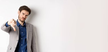 Olumsuz duygular. Hayal kırıklığına uğramış işadamı kaşlarını çatıyor, ürünleri onaylamıyor, kötü bir şeyden hoşlanmıyor, beyaz arka planda geziniyor..