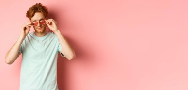 Yazın güneş gözlüklü yakışıklı kızıl adam kameraya küstah bakıyor, pembe arka planda duruyor..