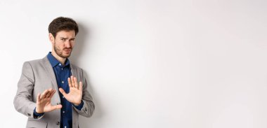 Uzak dur benden. İsteksiz işadamı endişeli bir yüz ifadesiyle geri adım atar, kötü teklifi engellemek için ellerini kaldırır, korkunç bir şeyi reddeder, hayır der ve teklifi reddeder, beyaz arka plan.