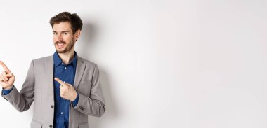 Gri takım elbiseli yakışıklı iş adamı logoyu işaret ediyor, reklamlara davet ediyor, beyaz arka planda duruyor..