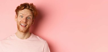 Komik kızıl saçlı adamın dil göstermesi, kameraya aptal suratlar yapması, pembe arka planda neşeli bir şekilde dikilmesi. Boşluğu kopyala