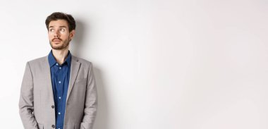 Takım elbiseli düşünceli üzgün işadamı sol üst köşedeki logoya bakıyor, düşünüyor veya uzaklaşıyor, beyaz arka planda duruyor..