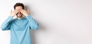 Gülümseyen beyaz adam sürpriz bekliyor, gözleri kapalı, hediye bekliyor, beyaz arka planda duruyor. Kutlama ve tatil kavramı.