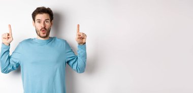 Şaşırmış genç bir adam en iyi reklamını yapıyor, yukarı bakıyor ve kameraya 