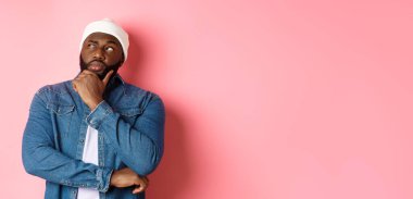 Düşünceli Afro-Amerikan erkek model karar veriyor, düşünüyor ve sol üst köşeye bakıyor, seçiyor ya da düşünüyor, pembe arka planda duruyor..