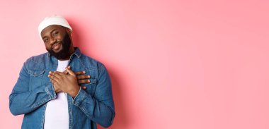 Minnettar ve dokunaklı siyahi adam teşekkür ediyor, gülümsüyor, çok sevimli ve yürekten el ele tutuşuyor, güzel bir jest yapıyor, pembe arka planda duruyor..