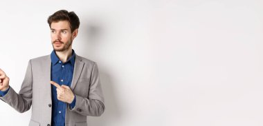 Takım elbiseli yakışıklı bir işadamı, ciddi bir yüzle logoya bakıyor, beyaz arka planda duruyor..