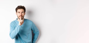 Çekici sakallı bir adam sessiz kalmak istiyor. Tabu işareti yapıyor. Sakin bir şekilde kameraya bakıyor..