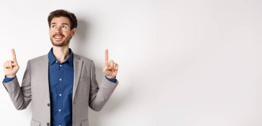 Takım elbiseli, gülümseyen, gülümseyen bir erkek yönetici, mutlu bir yüz, reklamlara bakıyor, beyaz arka planda duruyor..