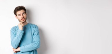 Yakışıklı genç bir adamın seçim yapması, düşünmesi, düşünmesi, bakması, beyaz arka planda durması..