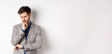 Takım elbiseli düşünceli bir işadamı, aşağı bakıp düşünüyor, karar veriyor, beyaz arka planda duruyor..