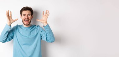 Korkmuş genç bir adamın el sıkışması, çığlık atması, kameraya bağırması hayal kırıklığına uğramış ya da endişeli, beyaz arka planda paniklemiş..