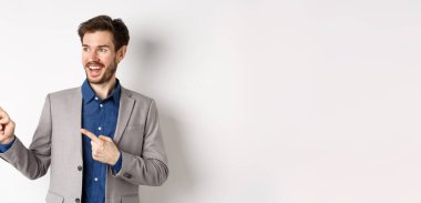 Heyecanlı, sakallı, şenlikli takım elbiseli, sola bakan, şaşkın bir şekilde gülümseyen, havalı reklam anlaşmaları yapan, beyaz arka planda duran adam..