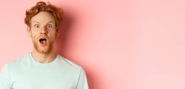 Şaşkın kızıl saçlı adamın tanıtım teklifine tepkisi, kaşlarını kaldırması ve nefes nefese kalması, kameraya huşu içinde bakması, pembe arka planda durması..