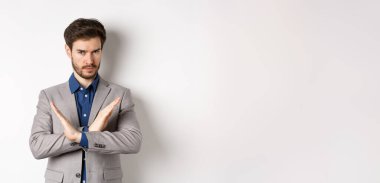 Ciddi bir iş adamı karşı çıkıyor ve hayır diyor, kararlı görünüyor, aynı fikirde değil ve kötü bir şeyi yasaklıyor, durmasını söyle, beyaz arka planda takım elbise içinde duruyor..