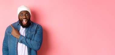 Şok olmuş ve baskı altında kalmış siyahi adam şikayet ediyor, kameraya bağırıyor ve sol üst köşedeki fotokopi alanını işaret ediyor, pembe arka planda duruyor..