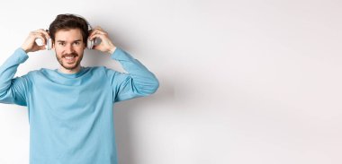 Adam müzik ya da podcast dinlemek için kablosuz kulaklık takmış, kameraya gülümsüyor, pembe arka planda duruyor..