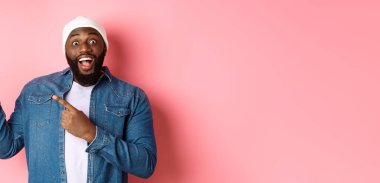 Harika bir tanıtım teklifi sunan siyahi adam, kameraya bakıyor, heyecanlı ve gülümsüyor, sol üst köşedeki afişi işaret ediyor, pembe arka plan..