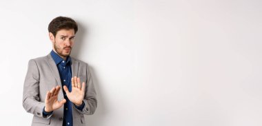 Uzak dur benden. İsteksiz işadamı endişeli bir yüz ifadesiyle geri adım atar, kötü teklifi engellemek için ellerini kaldırır, korkunç bir şeyi reddeder, hayır der ve teklifi reddeder, beyaz arka plan.