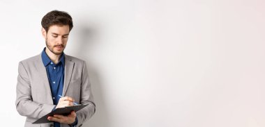 Takım elbiseli bir ofis çalışanı panoya yazı yazıyor, toplantı notları alıyor, beyaz arka planda duruyor..