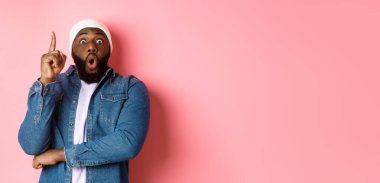 Yakışıklı hippi siyahi adamın bir fikri var, parmağını kaldırıp öneride bulunuyor, çözümü var, pembe arka planda duruyor..