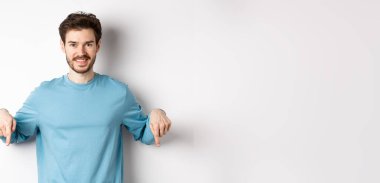 Gülümseyen, kendine güveni tam bir adam, beyaz arka planda reklam pankartı ya da logosu gösteriyor, mavi bir kazakla dikiliyor..