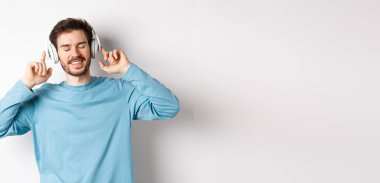 Kablosuz kulaklıkla müzik dinleyen yakışıklı bir adam ve gülümseyen, iyi sesin tadını çıkaran, beyaz arka plan.