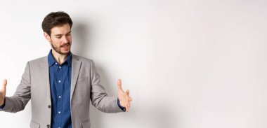 Heyecanlı yakışıklı iş adamı uzun boyda bir şey gösteriyor. Ellerini uzatıp beyaz arka planda duran büyük bir nesne..