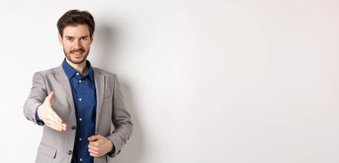 Kendine güvenen iş adamı elini uzatıp iş tokalaşması ve gülümseme için beyaz arka planda kendini tanıtır..