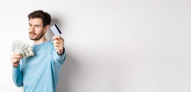 Ciddi görünümlü bir adam plastik kredi kartıyla elini uzatıyor, para yerine temassız ödemeyi tercih ediyor, beyaz arka planda duruyor..