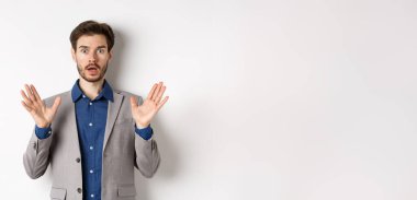 Süpriz takım elbiseli işadamı elini kaldırıyor ve heyecanlı görünüyor, beyaz arka plana karşı duruyor..