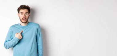 Şaşırmış genç adam soluk soluğa kalmış ve kendini inançsızlıkla işaret ediyor, seçilmiş ya da isimlendirilmiş, beyaz arka planda duruyor..