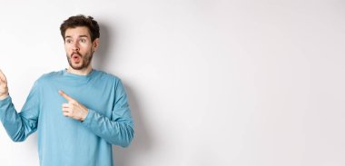 Vay canına, şuna bak. Etkilenmiş genç adam özel promosyon teklifini işaret ediyor ve sola bakıyor ya da beyaz arka planda indirimler, nefes nefese kalmış, stüdyoda duruyor..