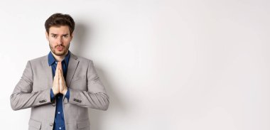 Üzgün yakışıklı iş adamının yardıma ihtiyacı var, lütfen ya da üzgünüm deyin, yalvarma hareketi yapın, iyilik isteyin, beyaz arka planda durun..