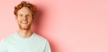 Sakallı, dağınık kızıl saçlı, beyaz dişli ve neşeli yüzlü pembe arka planda duran mutlu genç adam..