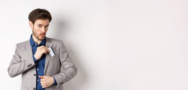 İş adamı kredi kartını takım elbisenin cebine koyar ve ıslık çalar, alışveriş yapar, beyaz arka planda durur..