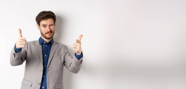 Sen halledersin. Beyaz takım elbiseli yakışıklı beyaz iş adamı kamerayı işaret ediyor ve göz kırpıyor, insanları motive ediyor, şirkette çalışmaya davet ediyor, beyaz arka planda duruyor..